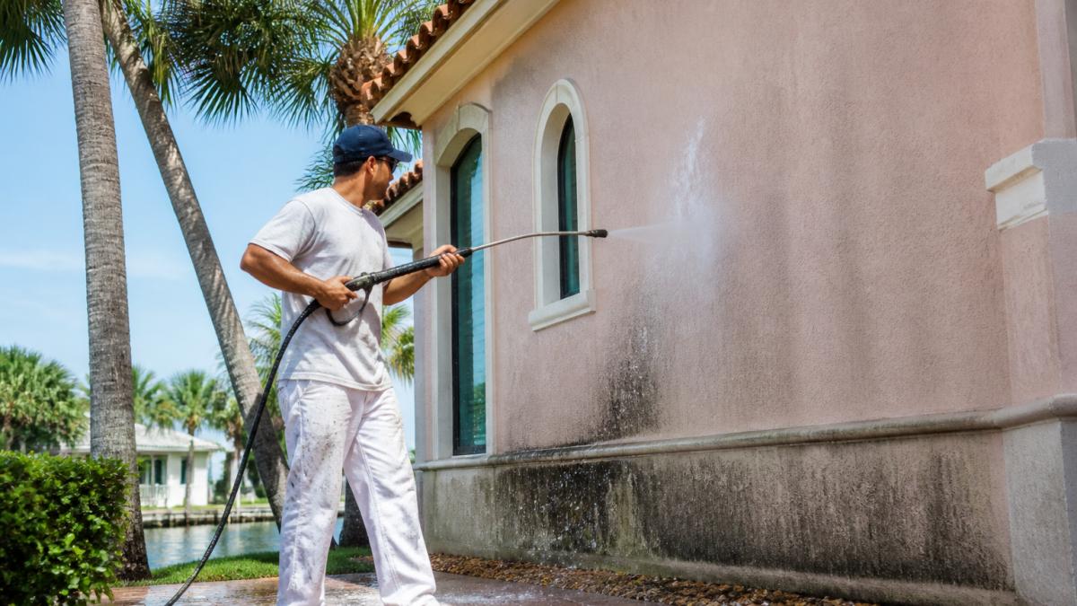 Painter pressure-washing a stucco wall to prepare for the best exterior paint for Florida humidity.