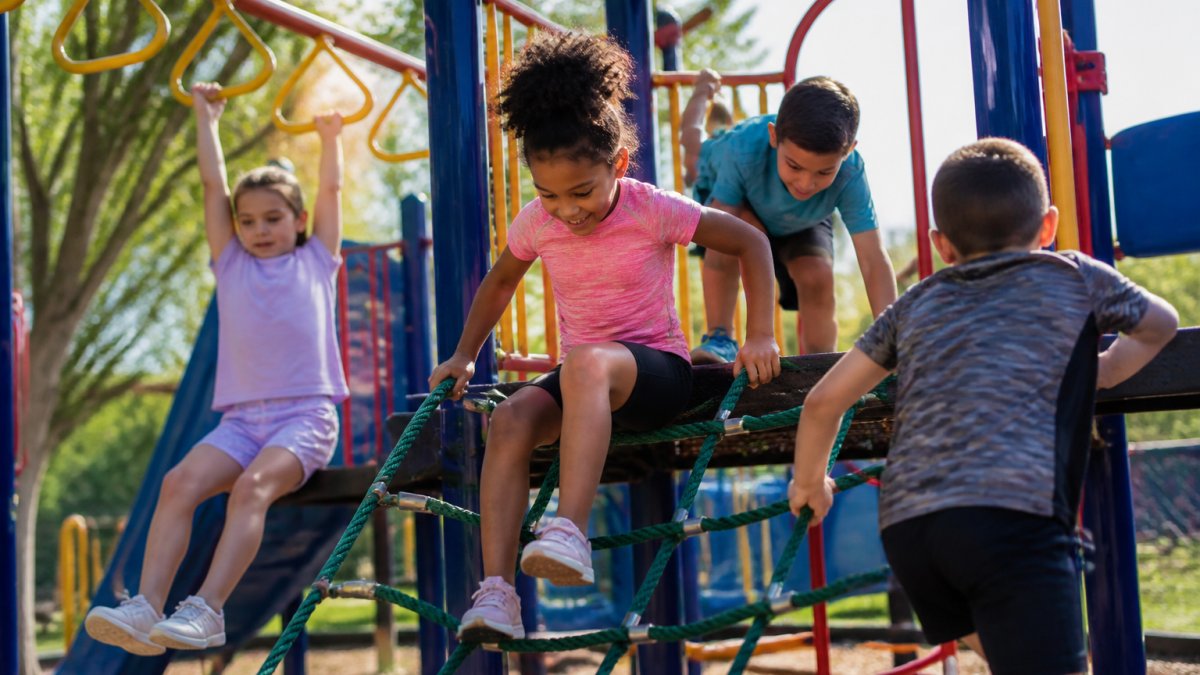 Children in colorful athletic wear running and climbing on outdoor playground equipment in bright sunlight