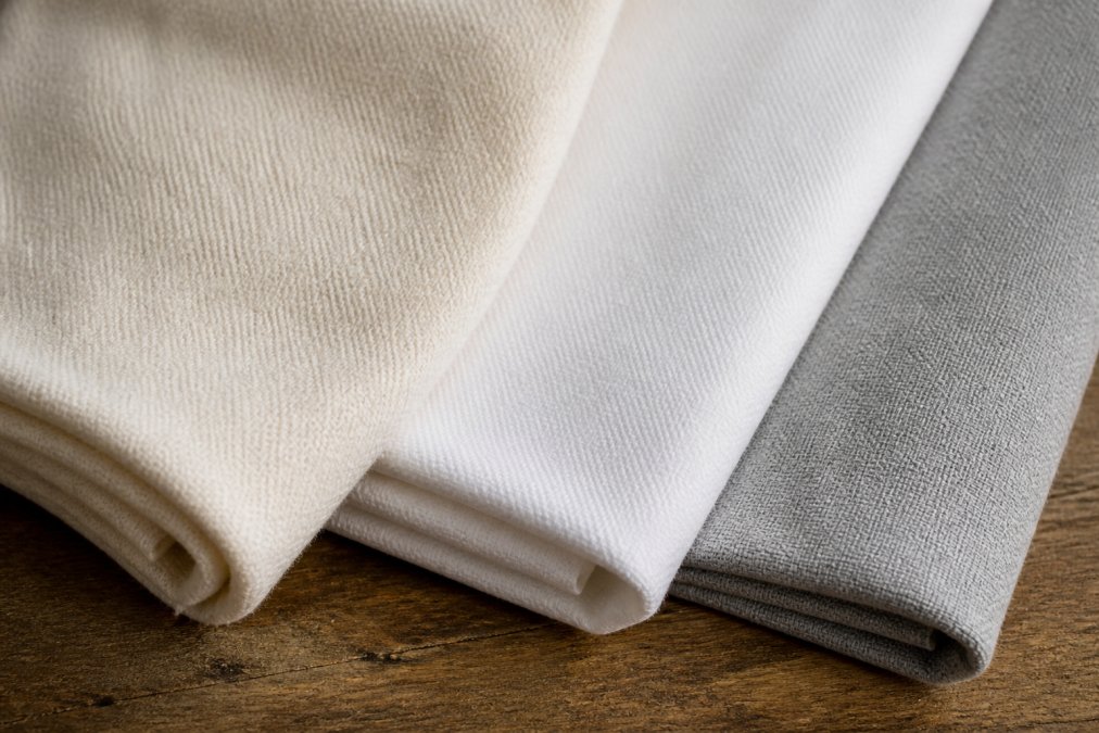 Close-up of folded fabric swatches showing cotton, polyester, and cotton-poly blend textures with visible weave differences and natural lighting