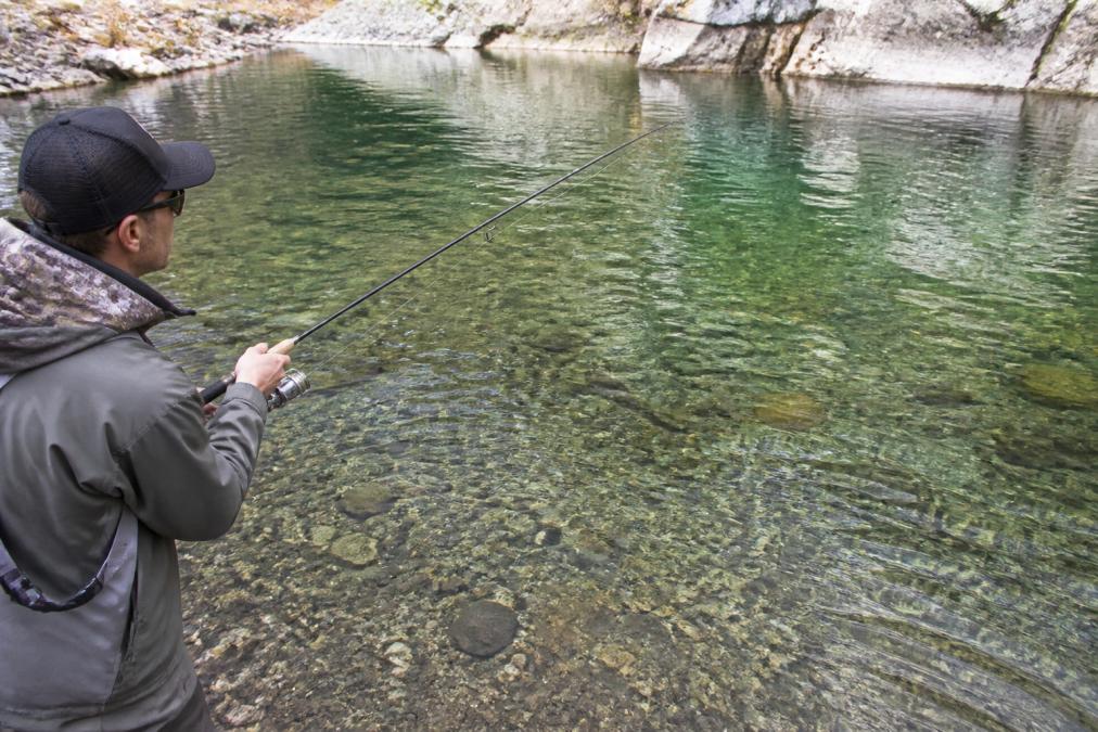 Angler holding spinning rod over clear water, demonstrating different line types visible in natural light conditions