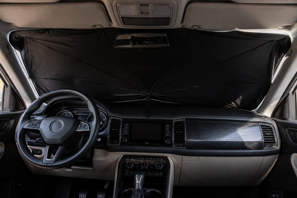 A car interior showing a deployed sun shade blocking bright sunlight through the windshield, with visible shadows cast across the dashboard and steering wheel on a hot afternoon