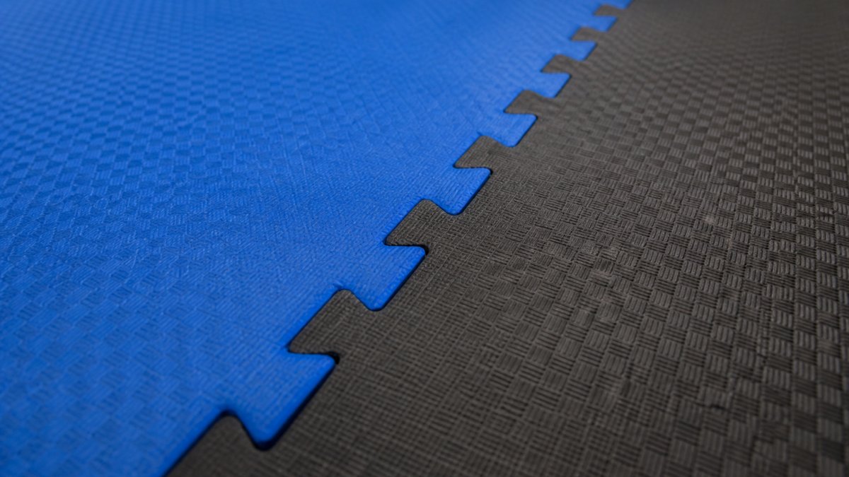 Close-up of interlocking foam puzzle mats laid out on a dojo floor, showing the connection points and textured surface used for martial arts training