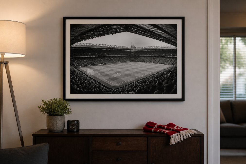 Framed black-and-white stadium photograph hanging above a dark wood sideboard in a warmly lit living room, with a folded red scarf resting on the surface below