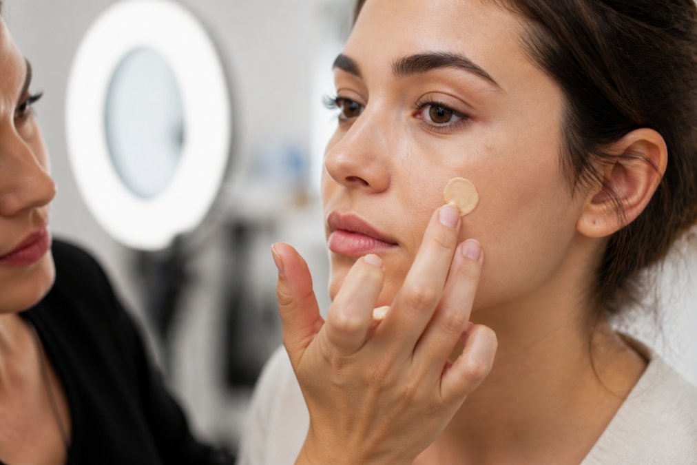 Makeup artist pressing a drop of thick foundation onto a client's cheek in a bright studio