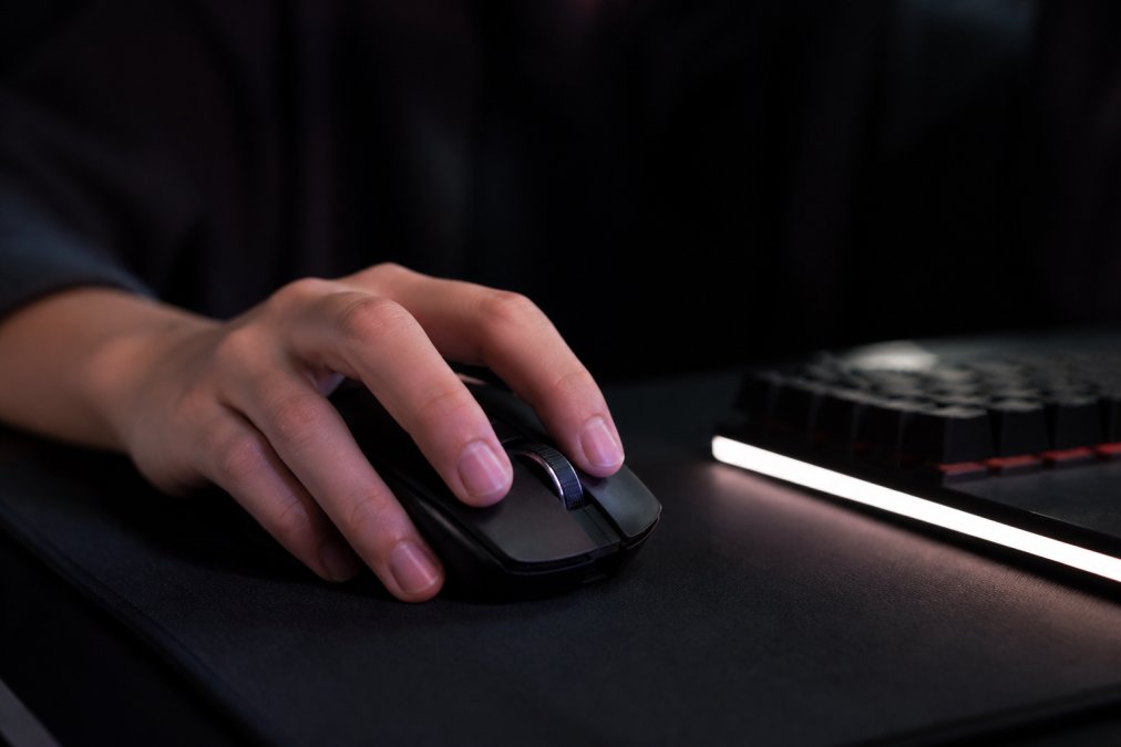 Close-up of a lightweight wireless gaming mouse on a dark desk mat, subtle RGB glow, a hand resting on it, dimly lit gaming setup