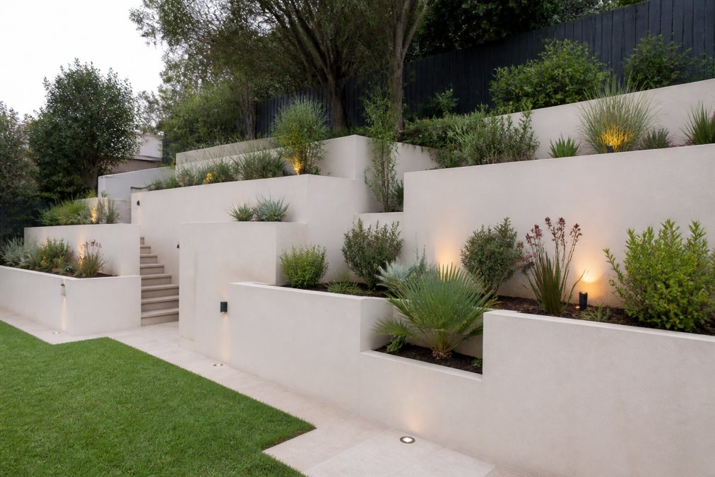 Well-constructed retaining wall in residential garden showing quality rendered blockwork, integrated planting pockets with native shrubs, terraced levels creating usable garden zones on sloped property