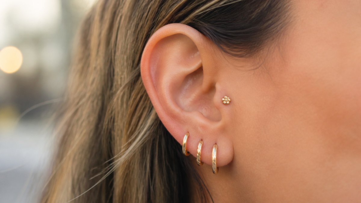 Close-up of a woman's ear wearing delicate 14K gold tragus earring, showing the jewelry against warm skin tone with natural side lighting highlighting the piece's craftsmanship