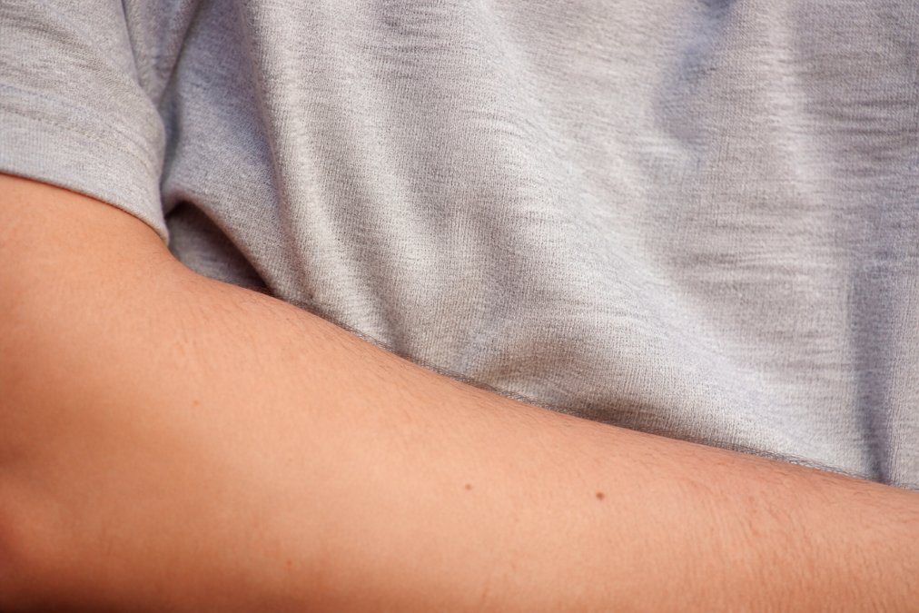 Close-up of a person's forearm resting against the smooth, heathered surface of a soft ring-spun cotton graphic tee, showing the fabric's texture in warm natural light