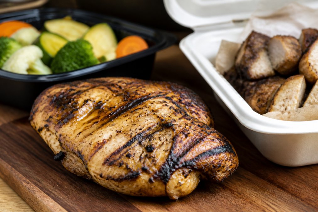 Freshly grilled chicken breast with char marks served as grilled takeout on a wooden board with mixed vegetables