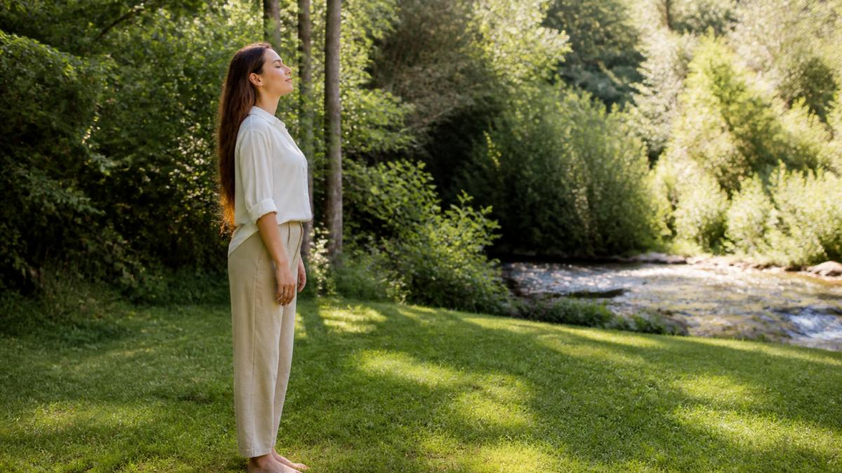 Person standing barefoot on grass in a natural outdoor setting, with visible peace and presence in their posture and expression, surrounded by green vegetation and natural light