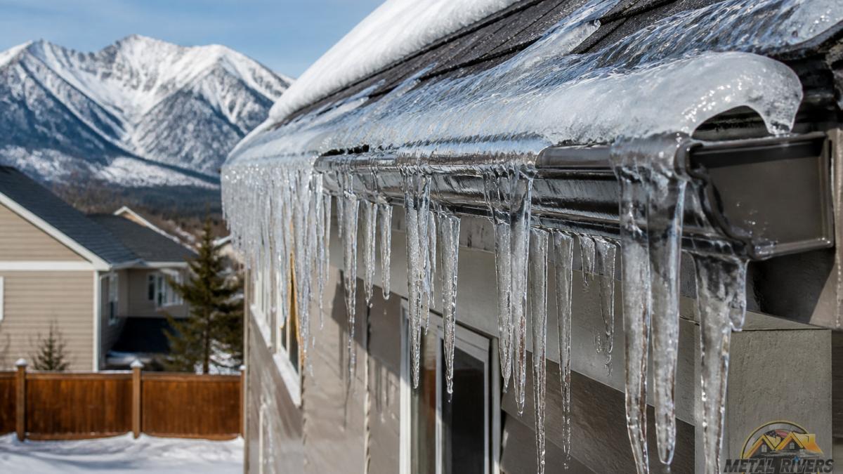 Close-up of thick icicles and ice dam formation hanging from a residential gutter on a snow-covered roof with frozen water backing up under shingles