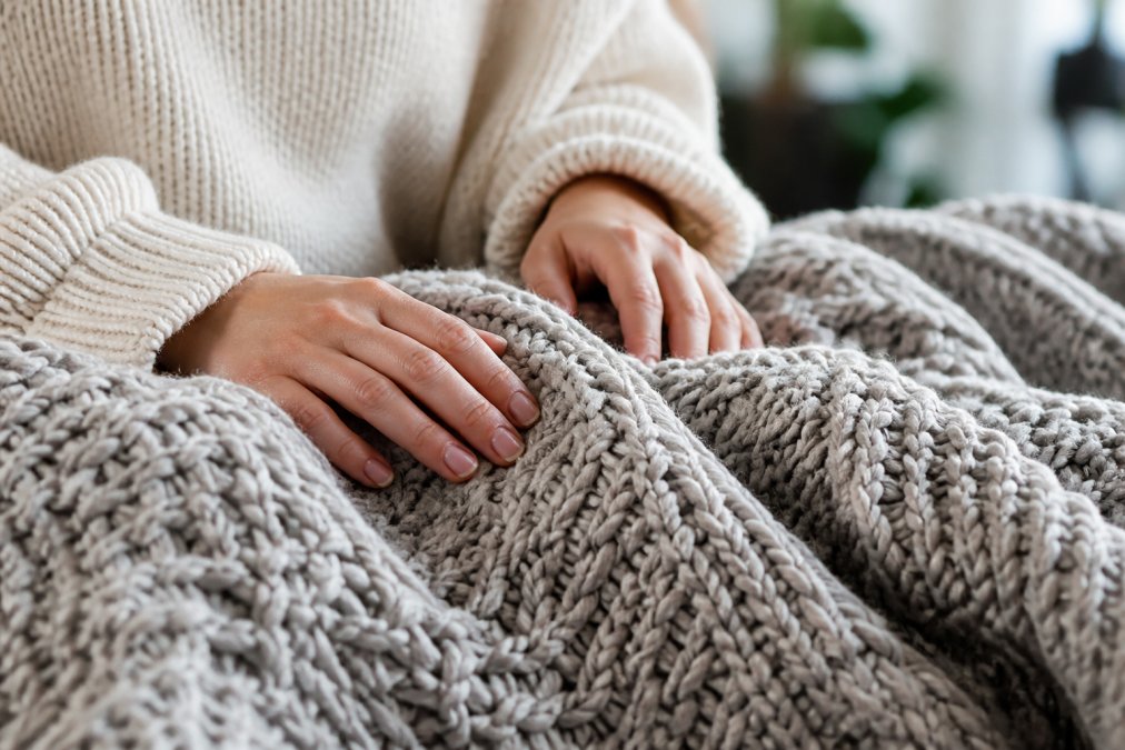 Close-up of hands gently touching a chunky knit blanket, showing intricate stitch patterns and textile depth in natural daylight