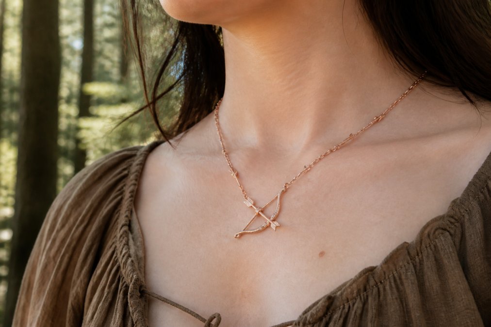Woman wearing a rose gold bow necklace and arrow chain, a piece of handmade jewelry styled with an earth-toned blouse.