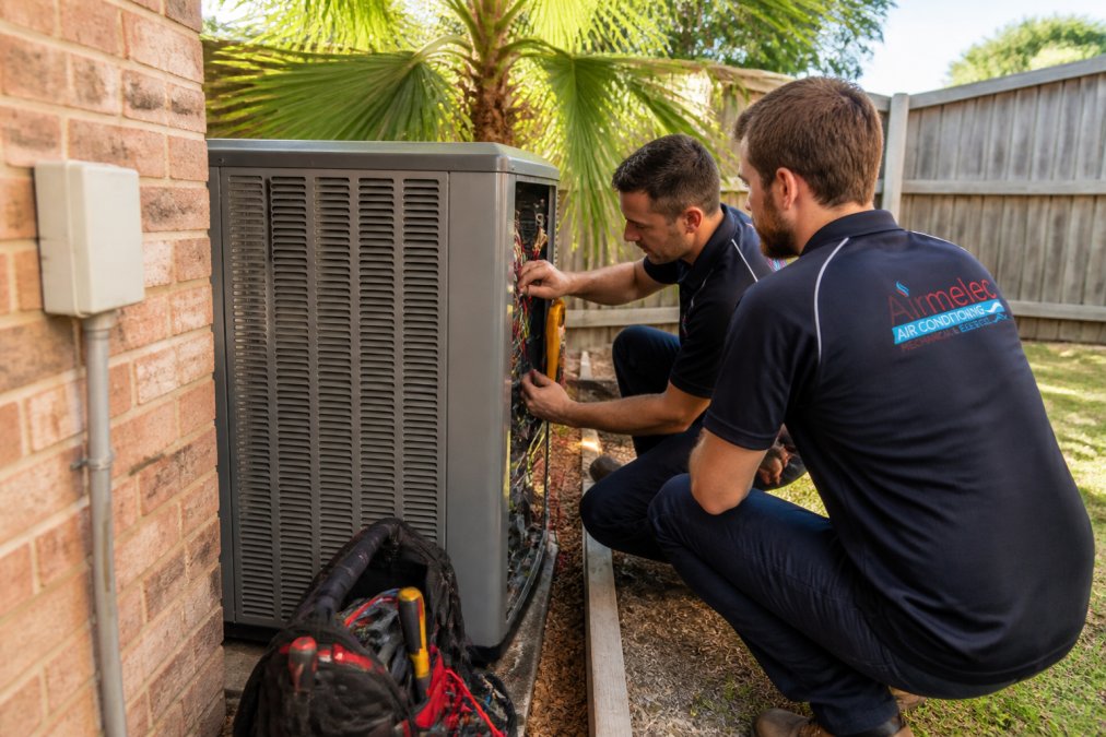 Licensed HVAC and electrical technicians repairing a residential AC unit as local contracting alternatives.