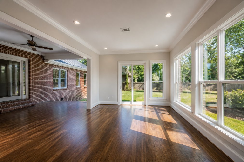 A bright, spacious newly constructed room addition with large windows connected seamlessly to an existing brick home in a suburban Jacksonville neighborhood, showing new hardwood flooring and abundant natural light