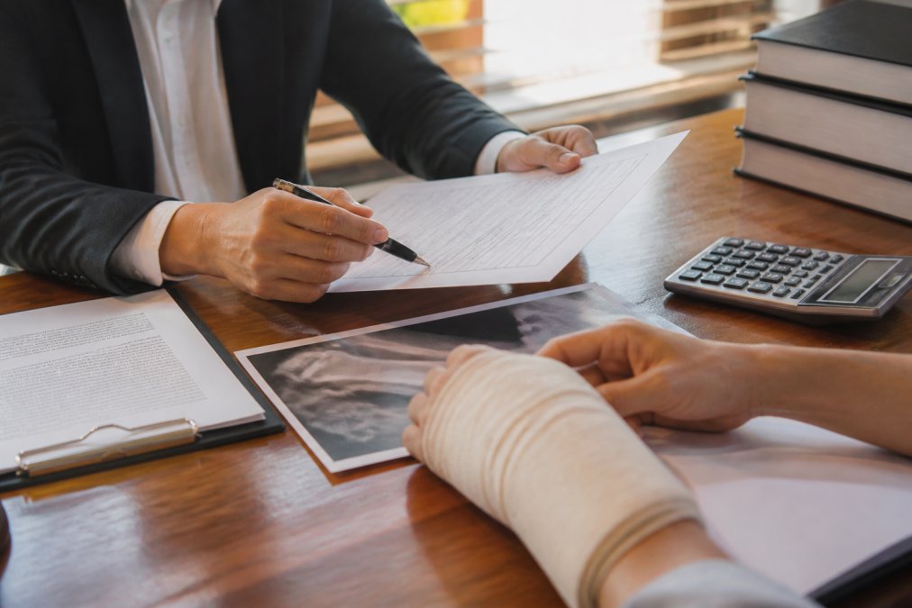 Close-up of hands reviewing medical documents and legal paperwork on desk with calculator and pen nearby, natural office lighting