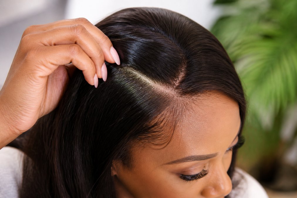 A woman gently parting her Remy human hair extensions to reveal a clean, healthy scalp underneath, with a visible monofilament base, shot in warm natural light to convey breathability and all-day comfort
