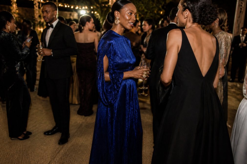 Woman wearing a royal blue metallic jacquard maxi dress with cut-out ruching detail on sleeves at an elegant evening gala, photographed in soft warm lighting that highlights the shimmering fabric and flowing silhouette