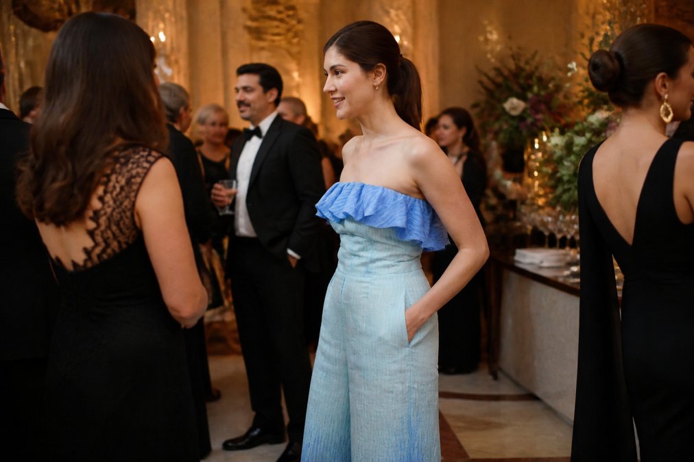 Woman wearing a strapless blue ombré organza jumpsuit at an upscale evening gala, photographed from the side to showcase the peplum waist and sculpted silhouette, with soft golden lighting highlighting the gradient fabric