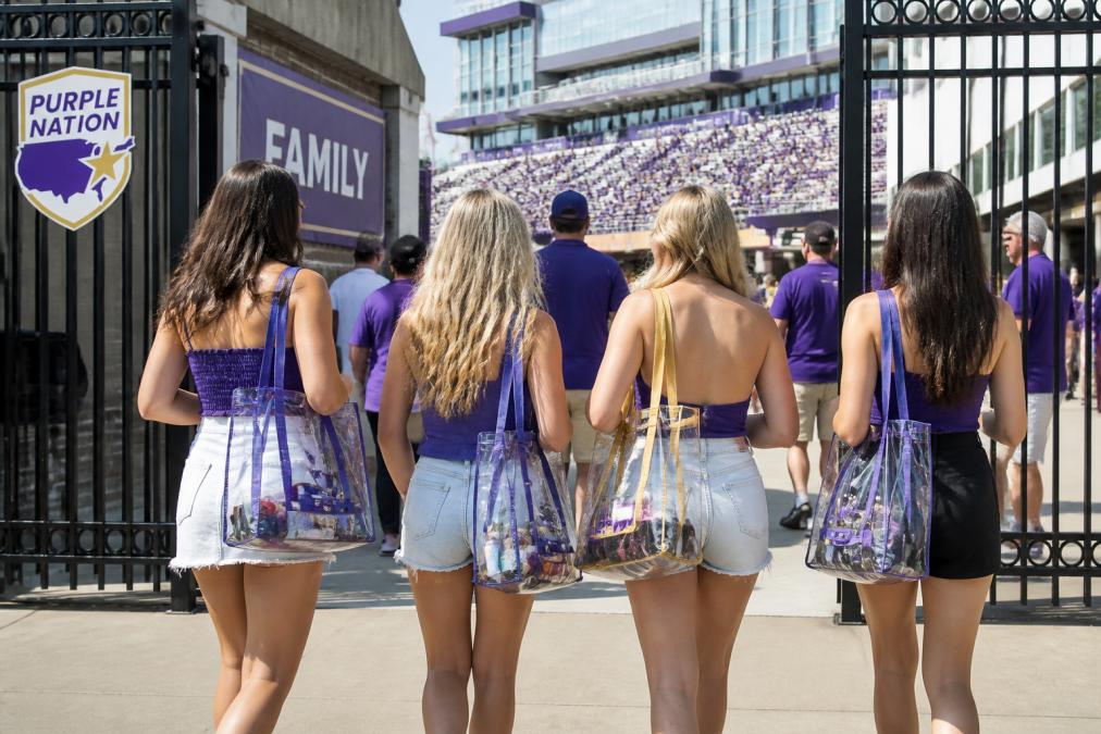 Group of JMU students walking through stadium gates with clear bags in purple and gold, showing stadium atmosphere and how bags look in real game day settings