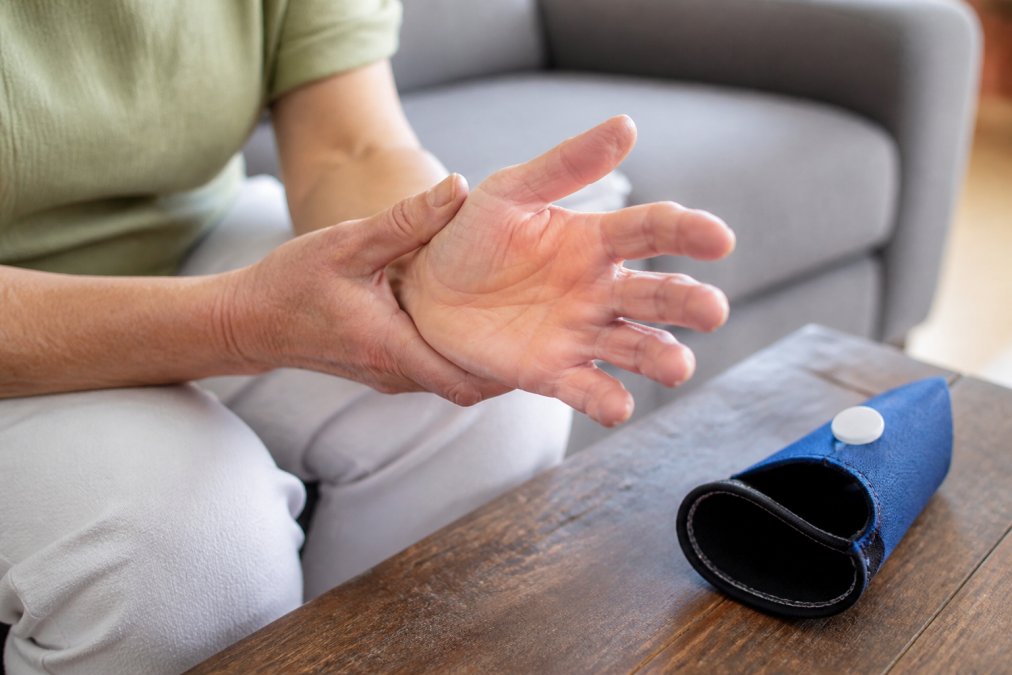 Close-up of a person in their 50s gently holding their arthritic hand, with a wearable cold compression sleeve nearby on a table