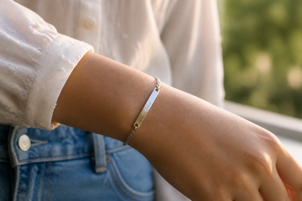 Woman's wrist displaying a personalized stainless steel bracelet with delicate engraved initials, worn during everyday activities with natural sunlight creating warm highlights on the metal
