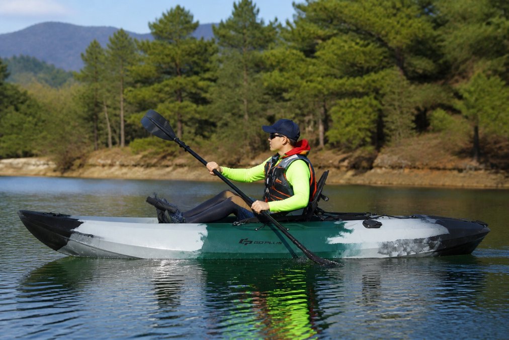 Kayaker wearing moisture-wicking base layers, a bright-colored quick-dry shirt, a properly fitted personal flotation device, and water shoes, paddling on calm water with proper posture and gear setup visible