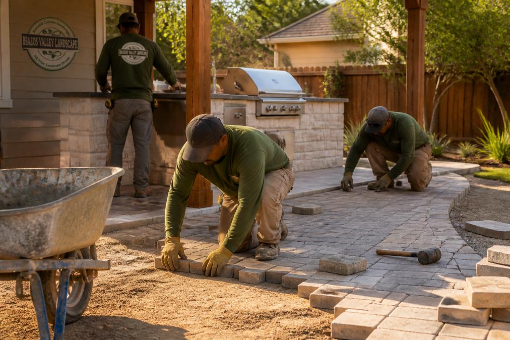 Professional landscape contractor crew installing a stone paver patio in a sunny residential backyard.