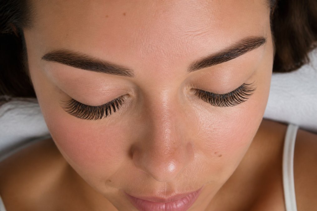 Close-up portrait of a woman with hooded eyes, eyes gently closed to reveal an open-eye lash mapping pattern with longer lashes at the center, photographed in soft natural window light