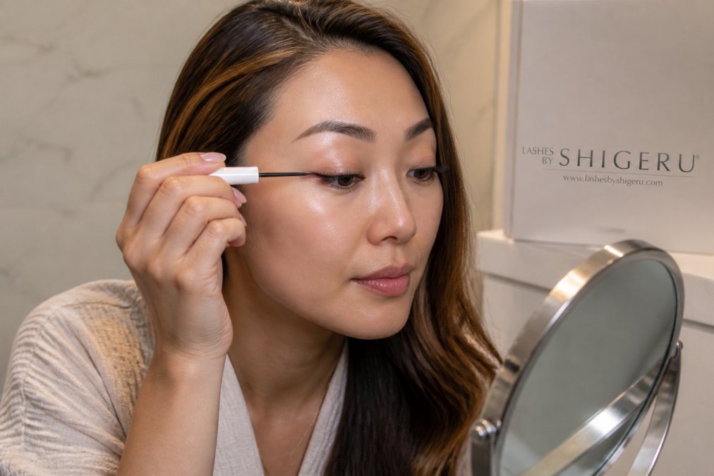 Woman carefully applying lash growth serum with a precise brush applicator to her lash line at home, demonstrating proper aftercare technique for maintaining extension health and strength