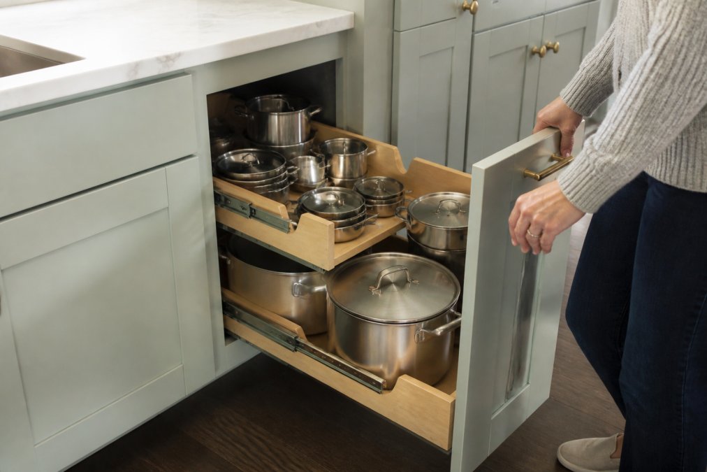 Person pulling out a sliding corner shelf filled with pots as one of the best lazy susan alternatives for kitchens.