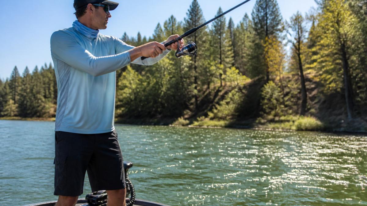 Angler wearing a long-sleeve breathable shirt casting from a boat on a sunny river with sparkling water