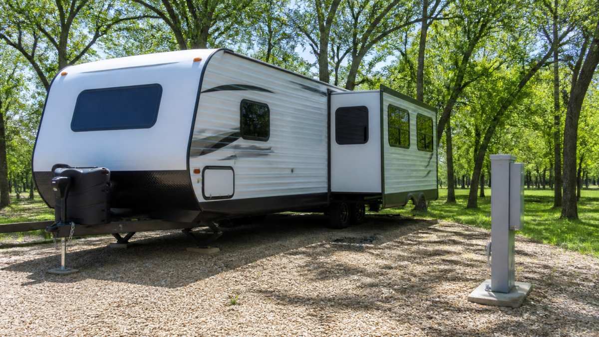 White travel trailer parked on a shady gravel site at one of the best long term rv parks weatherford in Texas.
