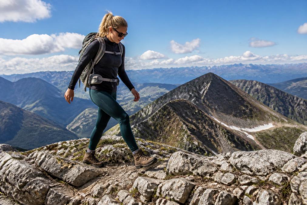 Female hiker navigating rocky alpine terrain wearing technical moisture-wicking leggings and a fitted performance top, moving confidently across exposed mountain ridge with dramatic landscape background