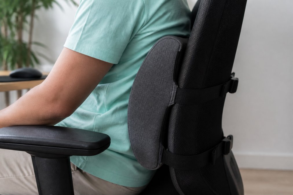 Close-up of lumbar support pillow attached to office chair, showing adjustable straps and proper placement against the lower back curve