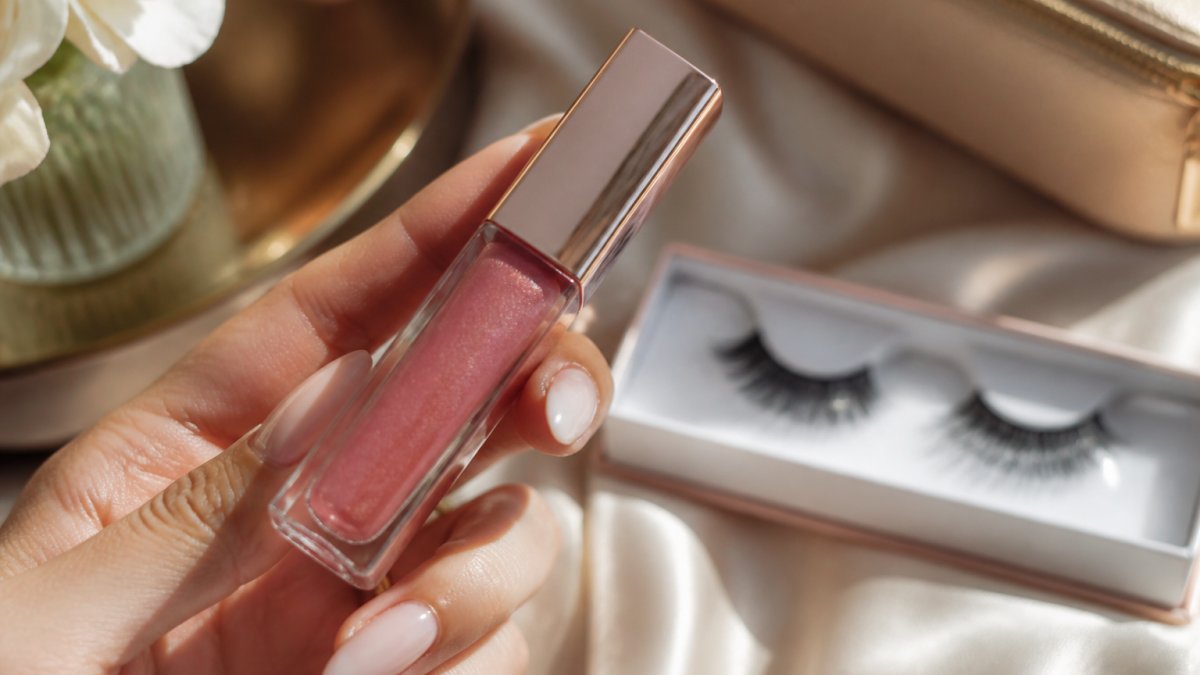 Close-up of a woman's hand holding a mirror-bright lip gloss with elegant packaging, soft natural light highlighting the high-shine finish