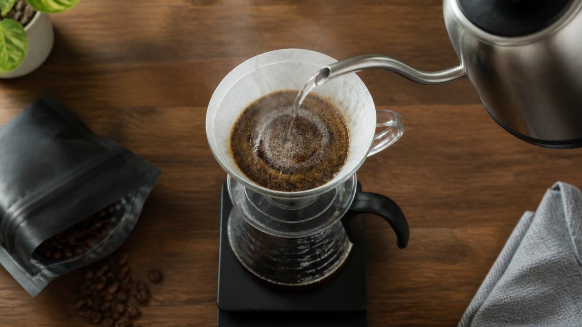 Gooseneck kettle pouring water over coffee grounds in a glass dripper on a kitchen scale