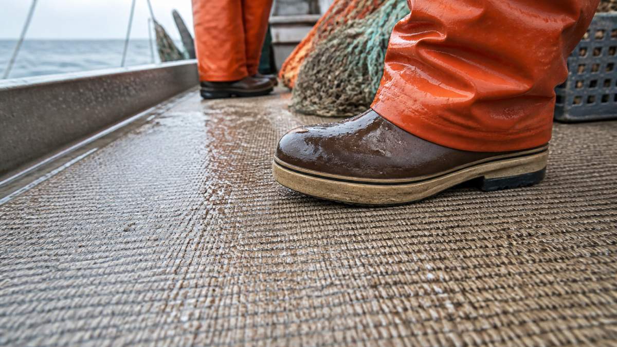 Close-up of a worker's boot gripping a textured woven vinyl boat deck surface with water droplets visible, showing traction on a commercial fishing vessel
