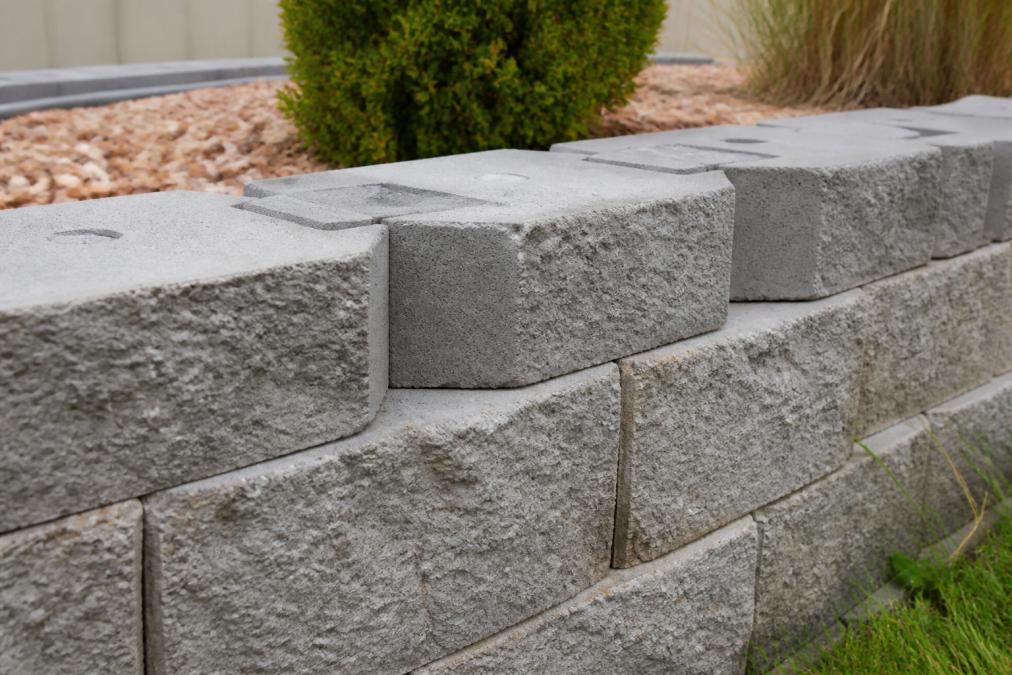 Close-up of interlocking concrete segmental retaining wall blocks stacked together showing textured gray surface and the mechanical locking system between blocks in a completed residential wall
