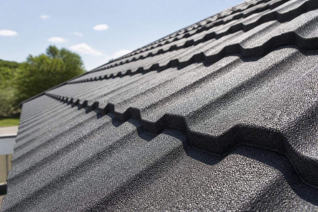 Close-up of a stone-coated metal roofing panel showing textured surface with reflective finish in bright sunlight, with the metal's sheen and color depth visible