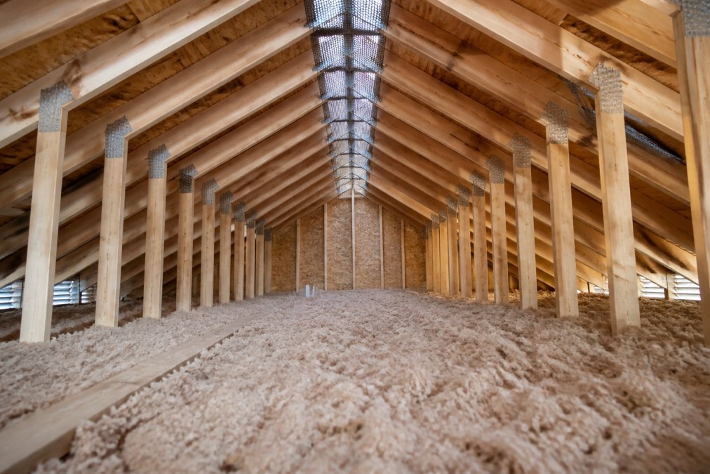 An attic space showing proper ventilation with ridge vents and soffit vents visible, demonstrating airflow paths with insulation layers below