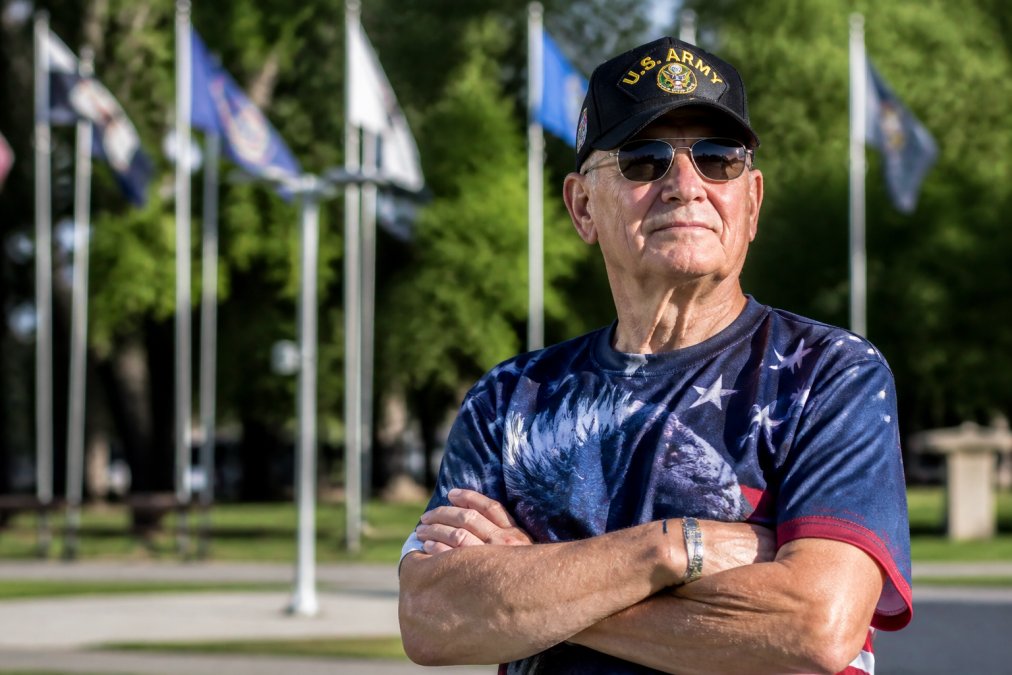 Retired veteran wearing branch-specific military cap and patriotic apparel standing outdoors with confident posture, showing pride in military heritage and service