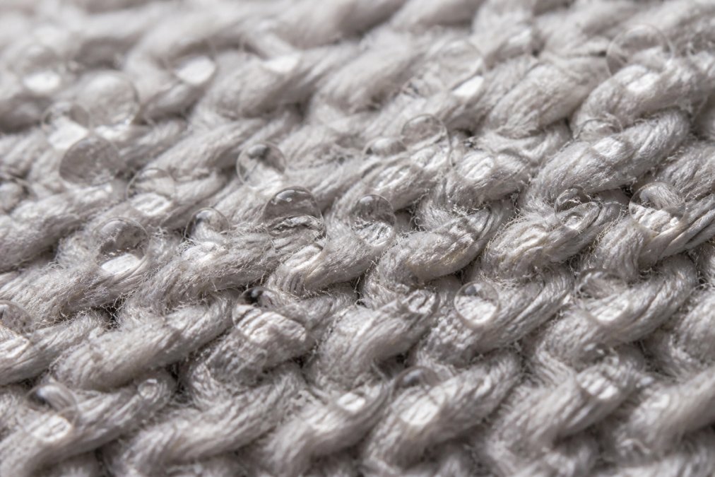 Close-up macro view of cotton-poly blend fabric weave showing the interlocking fibers, with visible moisture beading on the synthetic fiber surface demonstrating the hydrophobic properties that repel sweat