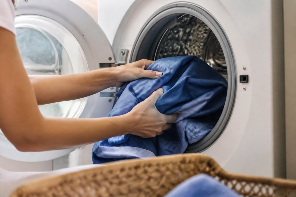 Hands carefully placing moisture-wicking scrubs into a washing machine, demonstrating proper handling and care of technical performance fabric