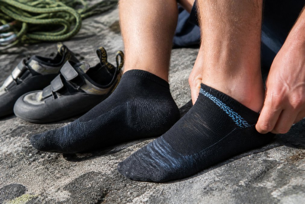 A climber's feet during a rest break on granite rock, showing sweat-dampened socks and the heel area where friction occurs, demonstrating real climbing conditions and sock performance