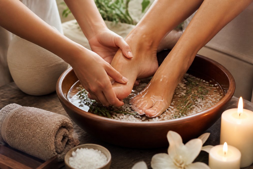 Person massaging tired feet in a warm herbal soak as one of the best natural products for foot health in a spa.
