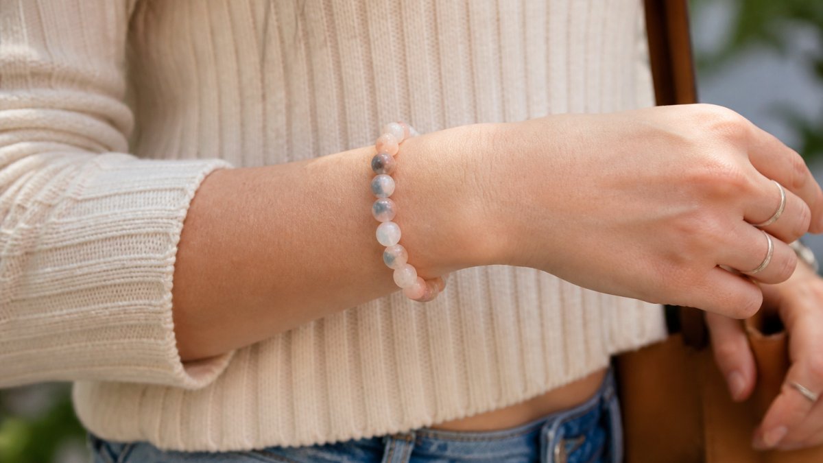 Close-up of a woman's wrist wearing a beaded natural stone bracelet in soft blue, pink, and peach tones, paired with casual everyday clothing, natural daylight
