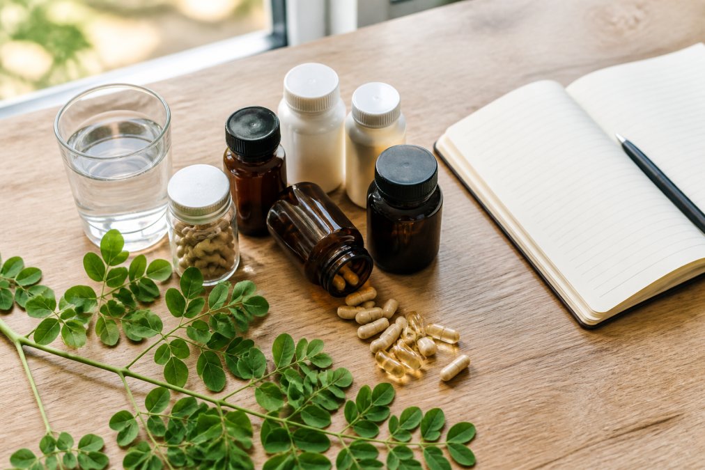 Comparison chart of natural energy supplements with moringa leaves, water, and a notebook on a wooden table