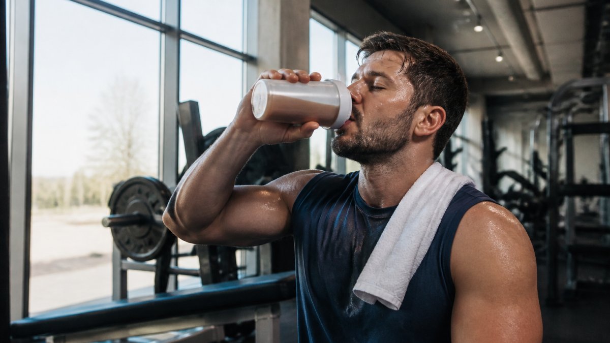 Athlete drinking a protein shake immediately after intense gym workout, focused expression, modern gym setting with natural lighting