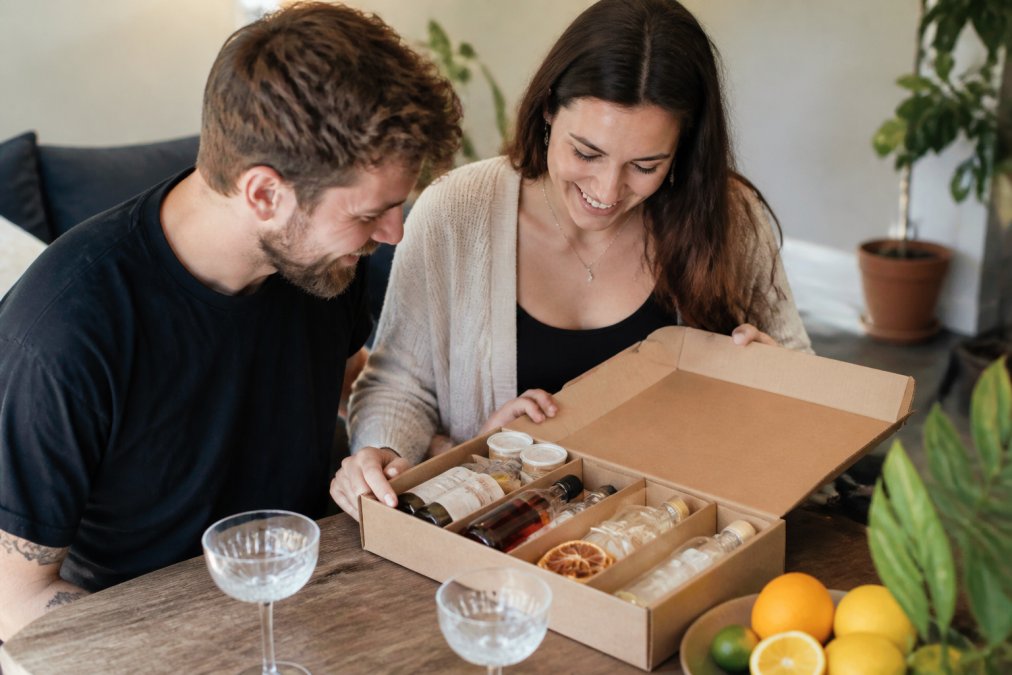 Premium cocktail gift box opened to reveal handcrafted garnishes, personalised label with recipient name, and premium spirit bottles arranged with serving glasses and fresh citrus
